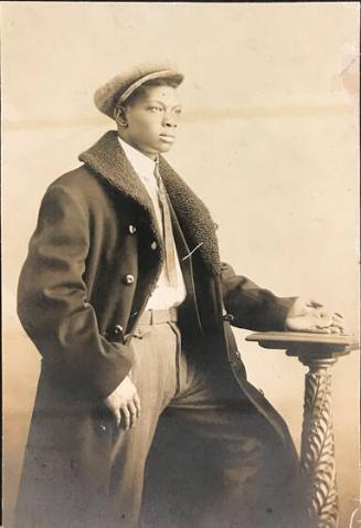 Three-quarter length portrait of an African-American man with hat and coat and hand on pedestal, holding pocket watch