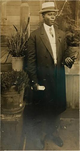 Full-length portrait of man in hat and coat holding book and rolled document