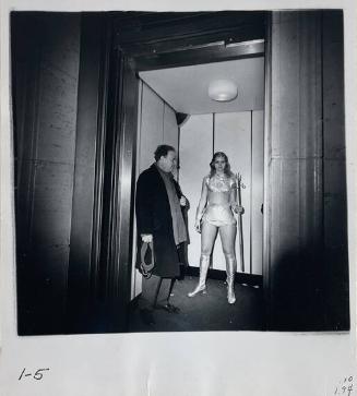Man Standing in an Elevator Next to a Woman Dressed in a Costume
