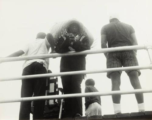 untitled (Haiti, a man in a feather headdress leaning on a railing with other men standing in the background)
