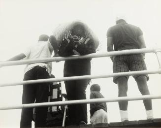 untitled (Haiti, a man in a feather headdress leaning on a railing with other men standing in the background)