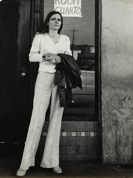 California (tall, thin woman in white in front of "rooms/cuartos" sign)