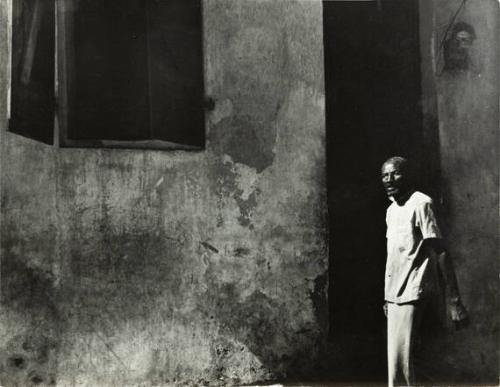 untitled (Haiti, man in white shirt standing against wall)