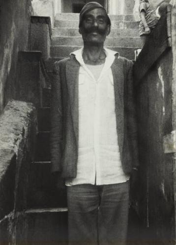 untitled (man wearing white shirt and cap standing in front of stairs mustache India)