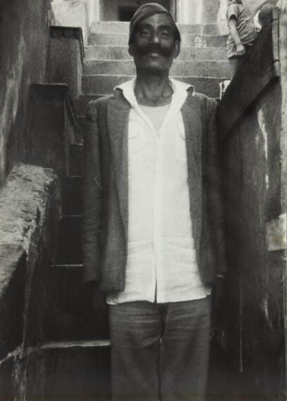 untitled (man wearing white shirt and cap standing in front of stairs mustache India)