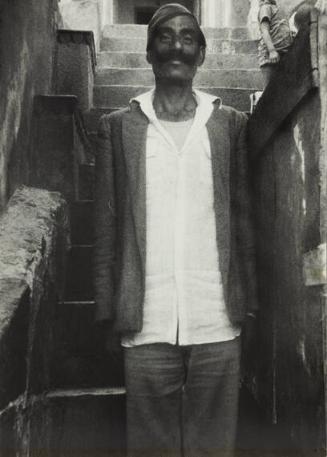 untitled (man wearing white shirt and cap standing in front of stairs mustache India)